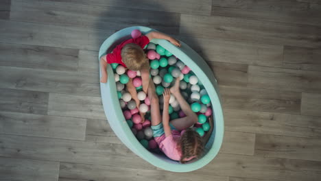 Little-brother-and-sister-sit-in-dry-pool-with-colored-balls