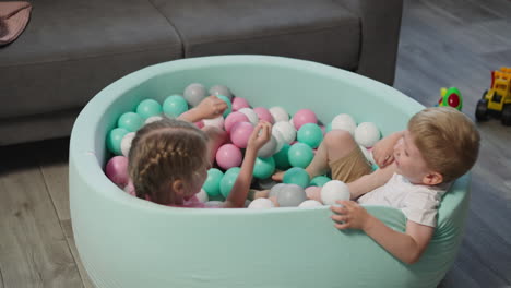 Little-girl-pulls-brother-leg-playing-in-pool-with-balls