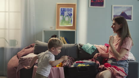 Boy-throws-toys-into-suitcase-woman-smiles-looking-at-son