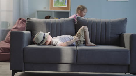 Boy-sleeps-on-couch-and-sister-pulls-suitcase-in-living-room