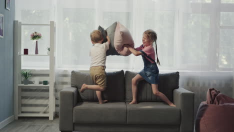 Brother-and-sister-fight-with-pillows-standing-on-soft-couch