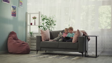 Children-watch-educational-cartoon-on-tablet-sitting-on-sofa