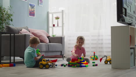 Mädchen-Baut-Haus-Aus-Blöcken,-Während-Junge-Mit-Spielzeug-Spielt