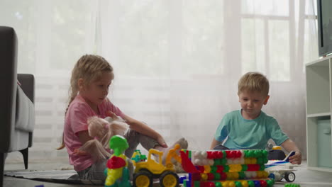 Toddler-throws-plastic-block-from-constructor-onto-sister