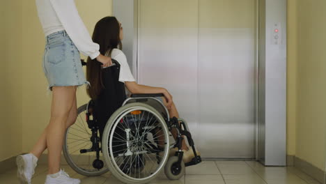 Woman-and-disabled-friend-in-wheelchair-stand-near-elevator
