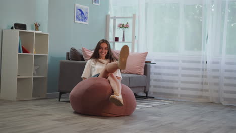 Cheerful-brunette-woman-falls-down-on-pink-bean-bag-chair