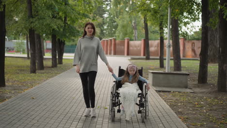 Little-girl-sits-in-wheelchair-holding-hand-of-caring-mother