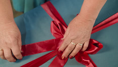 Hände-Einer-Frau,-Die-Ein-Rotes-Satinband-An-Eine-Blaue-Geschenkbox-Bindet