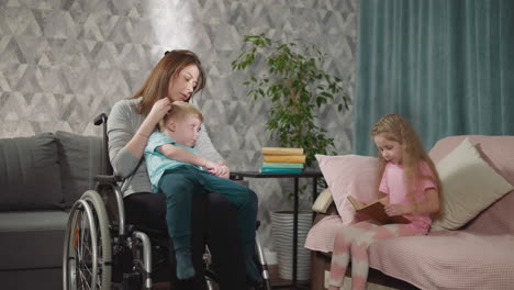 Kleines-Mädchen-Liest,-Während-Mutter-Ihr-Kleinkind-Im-Rollstuhl-Hält