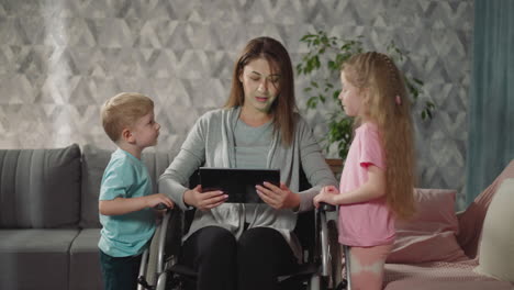 Children-stand-near-mother-in-wheelchair-watching-videos