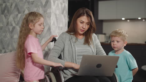 Focused-mother-talks-to-children-while-working-on-laptop