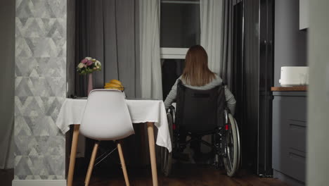 Frau-Rückt-Näher-An-Das-Fenster-Heran-Und-Dreht-Die-Räder-Ihres-Rollstuhls