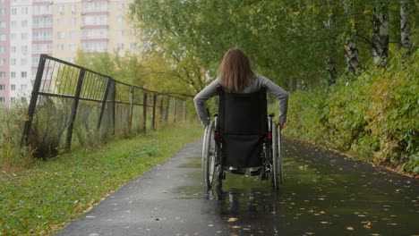 Female-in-wheelchair-walks-along-path-in-park-on-rainy-day