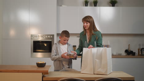 Mother-and-son-unpack-shopping-bags-with-food-in-kitchen