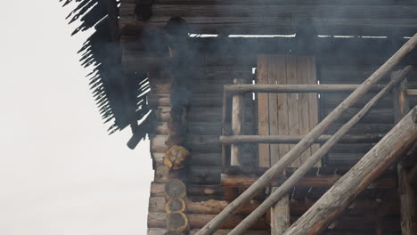 Smoke-rises-up-in-front-of-wooden-house-with-burnt-roof