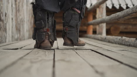 Man-in-heavy-boots-walks-along-wooden-platform-past-fence