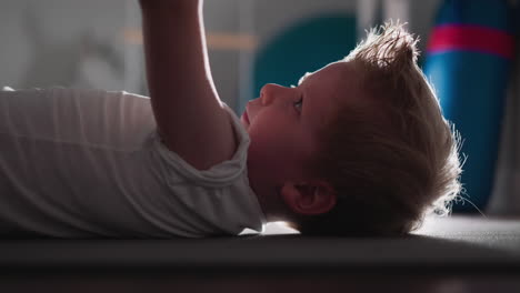 Focused-toddler-lying-on-floor-lifting-barbell-with-hands
