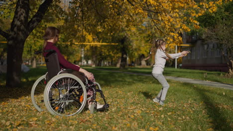 Frau-Mit-Behinderung-Schaut-Sich-Das-Mädchen-An,-Das-Mit-Blättern-Tanzt
