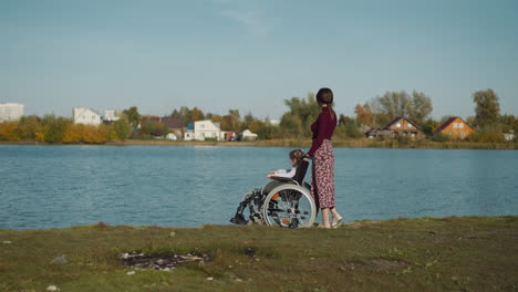 Mother-and-daughter-in-wheelchair-walk-on-shore-of-lake