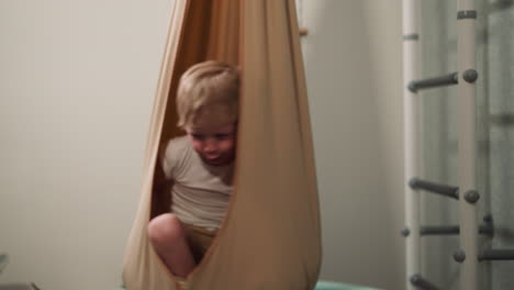 Happy-little-boy-sits-in-turning-hammock-chair-in-home-gym