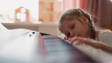 Little-girl-with-plaits-presses-piano-keys-in-living-room