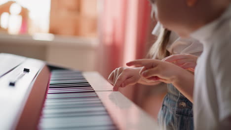 Toddler-boy-presses-piano-keys-after-elder-sister-at-home
