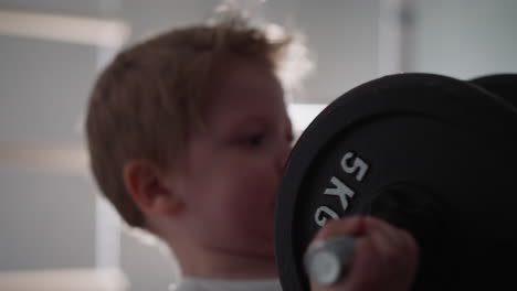 Chubby-toddler-lifts-heavy-barbell-to-pump-up-arm-muscles