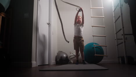Boy-hits-battle-rope-on-floor-standing-near-gym-equipment