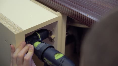 Furniture-maker-drills-the-side-surface-of-the-cabinet-using-a-corner-nozzle-on-the-drill-Close-up