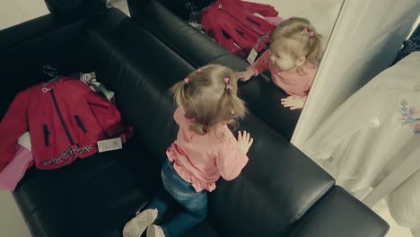 Kleines-Mädchen-In-Einem-Bekleidungsgeschäft-Sitzt-Auf-Der-Couch-Vor-Einem-Spiegel