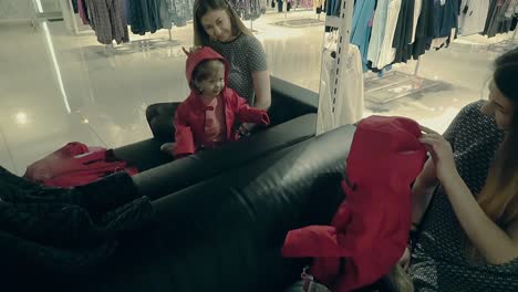 young-beautiful-mother-with-a-cute-baby-girl-in-the-store-trying-on-clothes-in-front-of-a-mirror