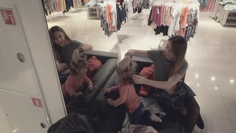 young-beautiful-mother-with-a-little-daughter-child-in-a-clothing-store-looks-in-the-mirror-mom-corrects-pigtails