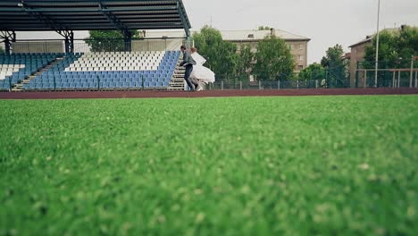 bride-and-groom-are-running-along-the-treadmill-at-the-stadium-the-green-grass