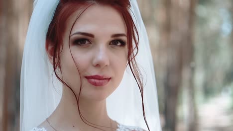 Portrait-of-a-bride-in-a-forest-in-a-wedding-dress-that-touches-a-curl-of-her-hair-smiling-close-up-slow-motion