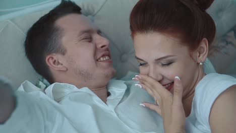 Young-beautiful-couple-resting-in-bed-laughing-yawning-close-up-slow-motion