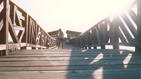 Young-beautiful-mother-goes-with-a-child-on-a-wooden-bridge-during-sunset