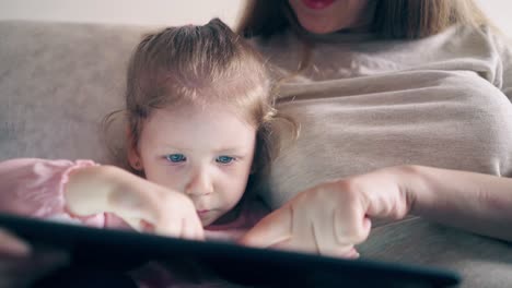 CU-4k-Young-attractive-mother-and-sweet-daughter-are-sitting-on-the-couch-and-teaching-using-a-tablet-computer