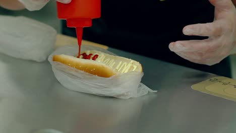 CU-Slow-motion-Cook-prepares-a-hot-dog-pours-a-red-ketchup-on-a-loaf