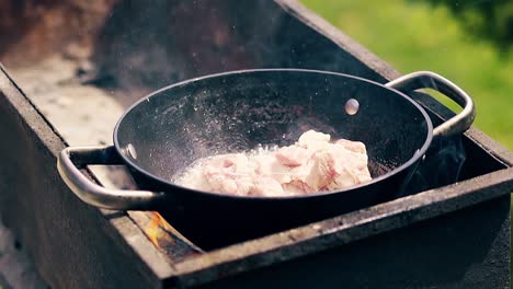 Close-up-Slow-motion-Pork-meat-is-fried-in-saucepan-on-charcoal-The-person-adds-meat-to-the-cauldron