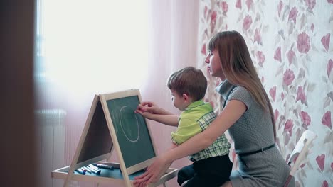 Mom-helps-son-to-draw-a-circle-on-blackboard