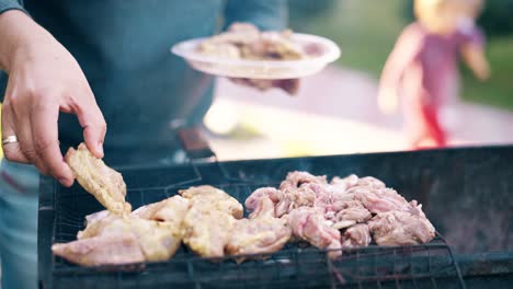 Close-up-Man-stands-on-the-background-of-a-summer-house-lays-meat-on-a-barbecue-grill-children-run-alongside