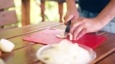 Close-up-The-guy-is-cooking-pilaf-He-is-in-a-summer-house-cuts-onions-on-a-red-cutting-board