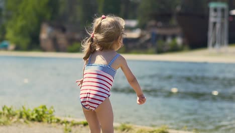 Close-up-Slow-motion-Little-girl-in-bathing-suit-throws-stone-at-lake-on-beach