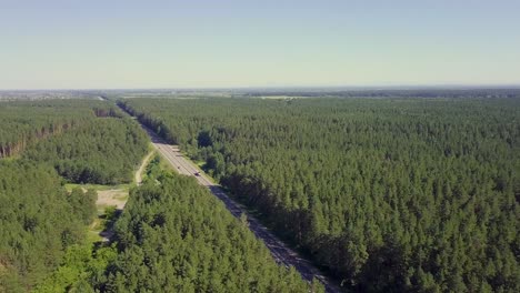 Aerial-Cars-move-along-the-highway-through-coniferous-forest-In-the-distance-you-can-see-the-fields-the-villages