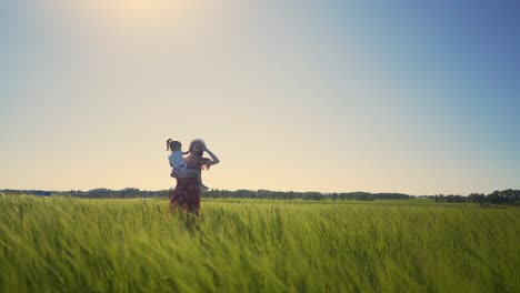 Mom-in-summer-hat-and-dress-in-field-holds-little-daughter-in-her-arms