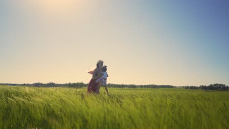 Mom-in-summer-dress-in-field-is-holding-little-daughter-Their-hair-and-dress-fluttering-in-wind