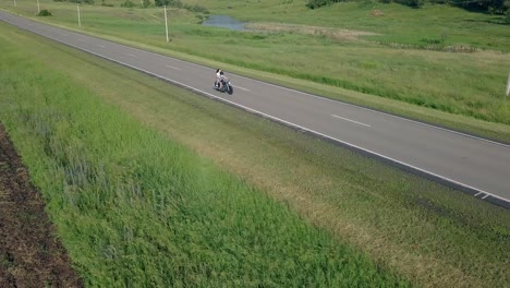 aerial-view-couple-on-black-motorcycle-drives-along-road
