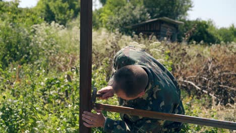 man-checks-welded-fence-parts-tapping-with-hammer-in-weeds