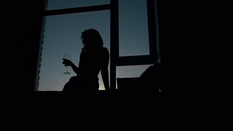 Silhouette-Einer-Frau-Mit-Einem-Glas-Wein-Auf-Der-Fensterbank