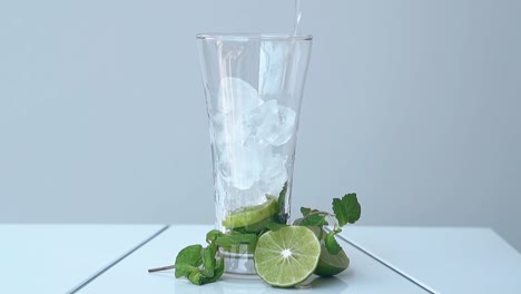 glass-with-lime-and-ice-cubes-stands-on-white-table-at-wall